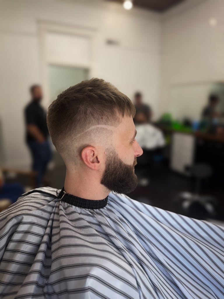 Man with short faded haircut and beard wearing striped cape in salon with blurred background