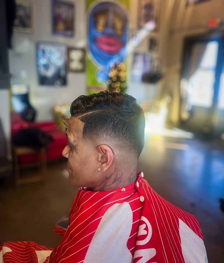 Person viewed from behind in a barbershop showing a fresh fade haircut with styled dark hair, wearing a red and white striped cape