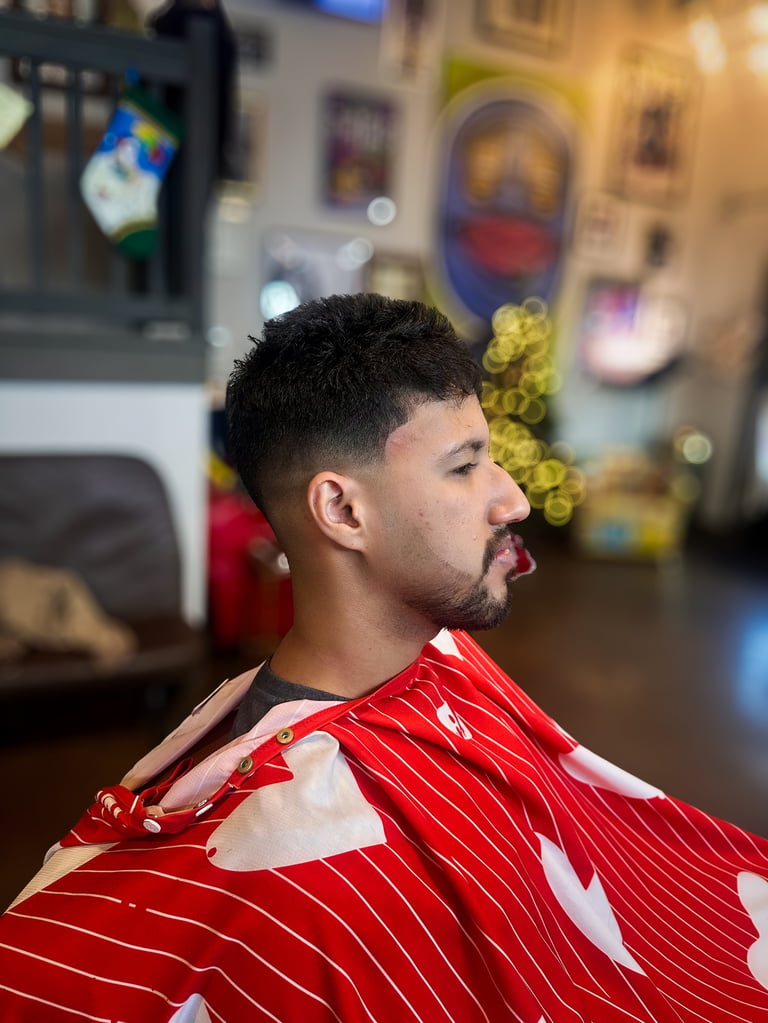 Man in profile wearing red and white pinstriped cape in a barbershop with blurred salon decor in background