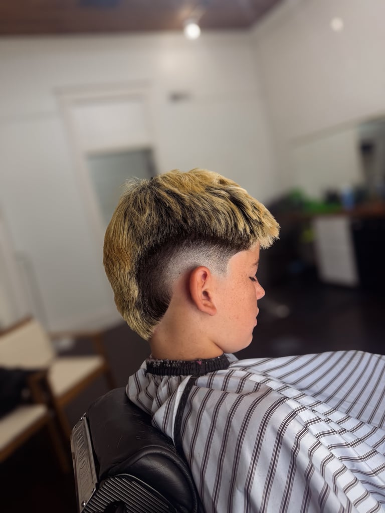 Person showing a short blonde and dark undercut hairstyle from the side, wearing a striped shirt in a salon setting