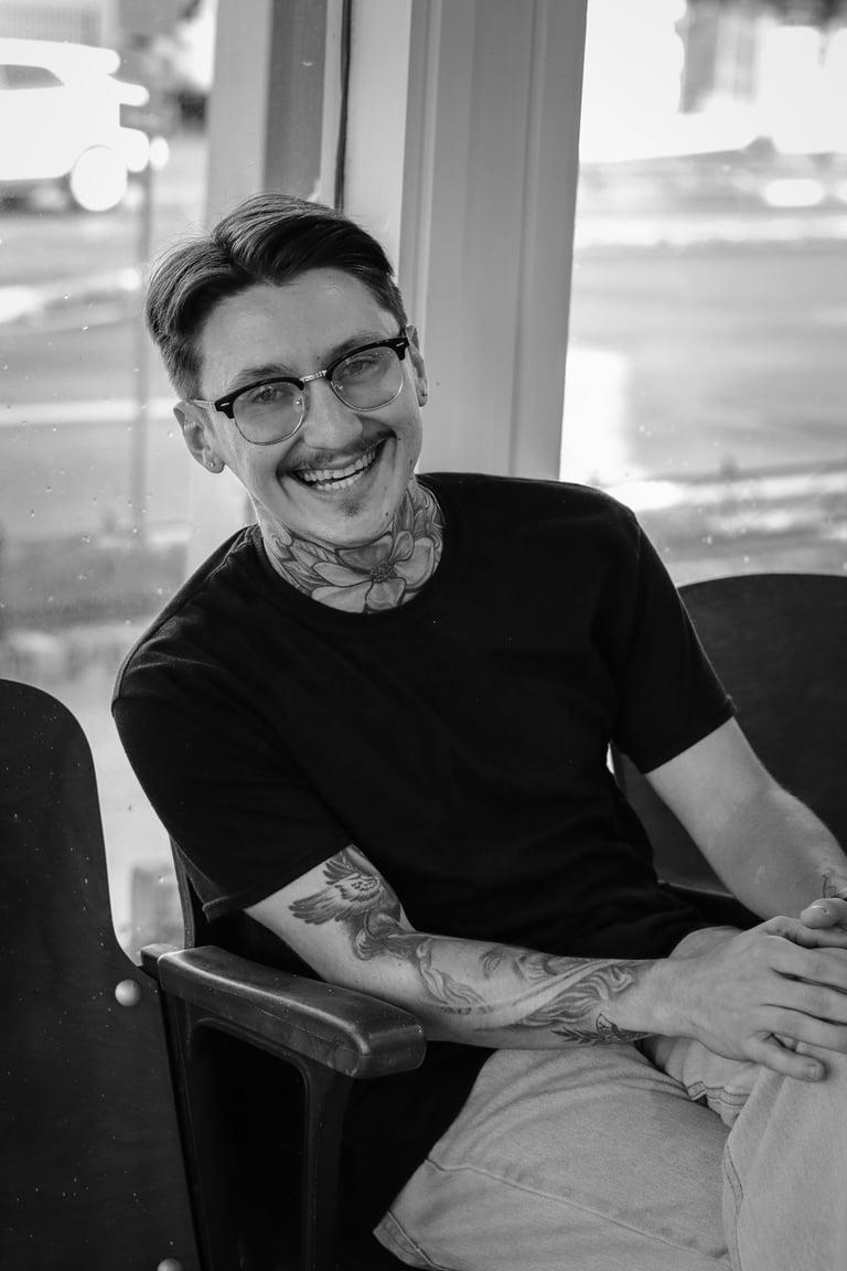 Dillon Johnson - Owner and Tattoo Artist - smiling man with glasses and tattoos in black and white portrait